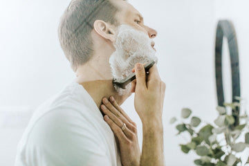 Man shaving his beard with an electric shaver in a bathroom