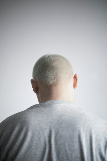a man with a bald head standing in front of a white wall